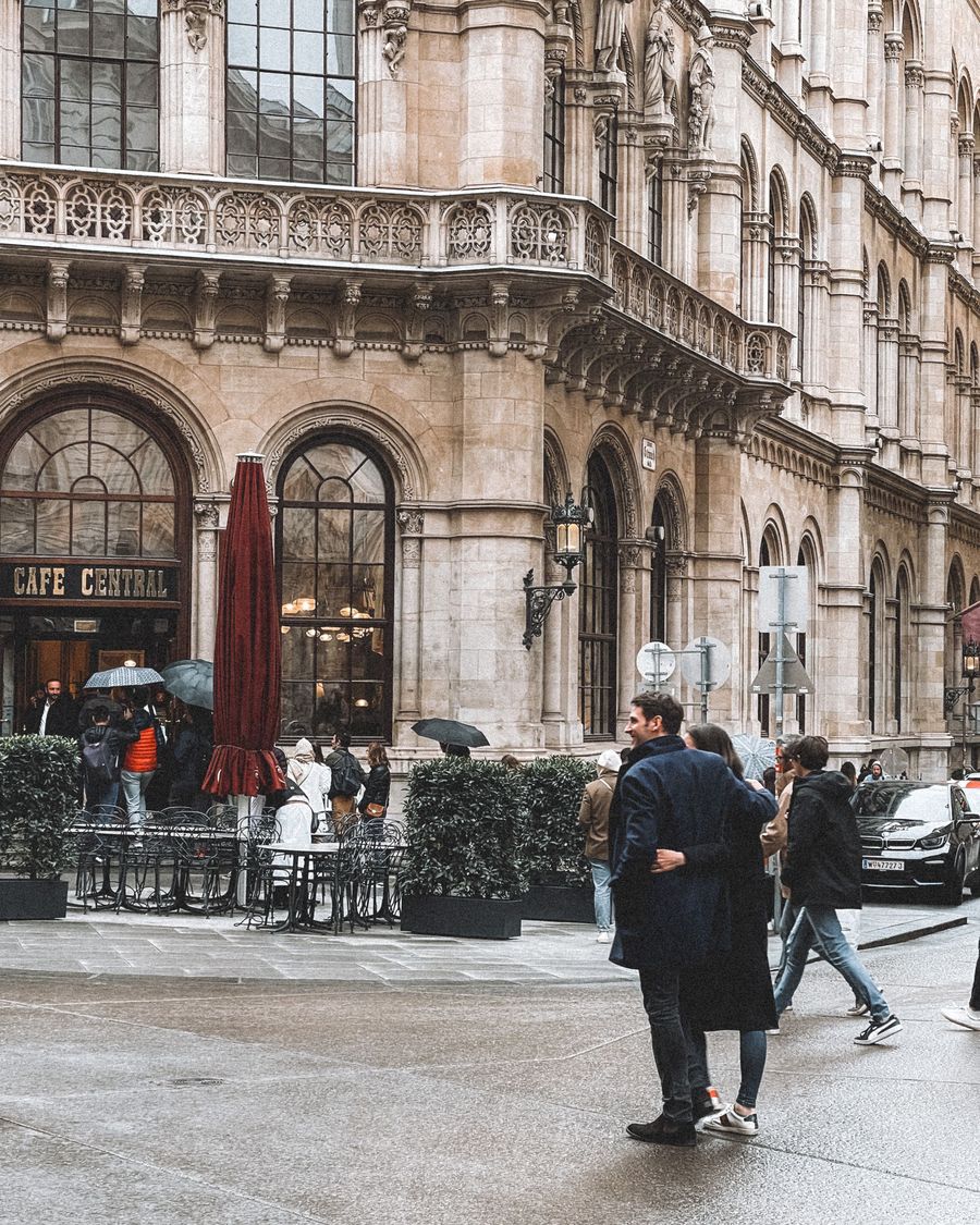 People walking past the arched windows of Café Central on a rainy day in Vienna