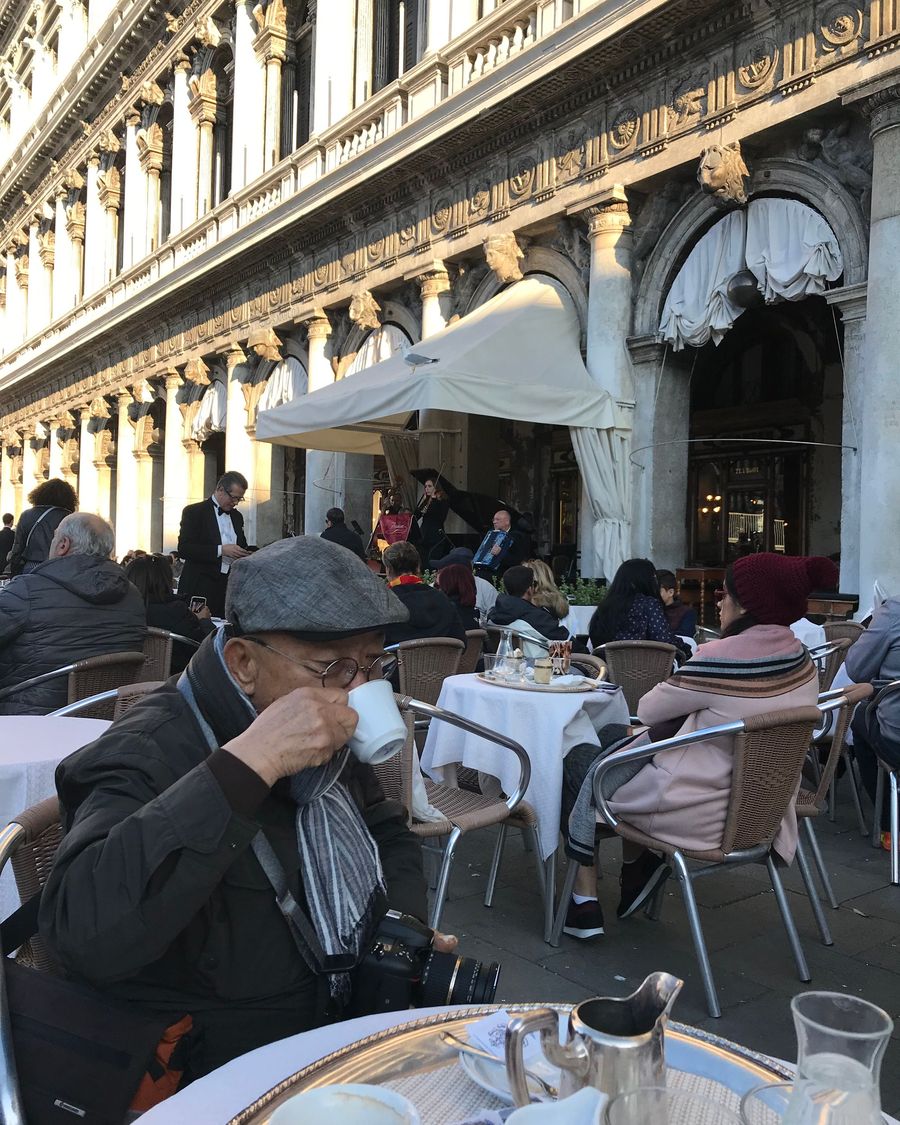A man sips coffee at an outdoor table under the arcades of Caffè Florian