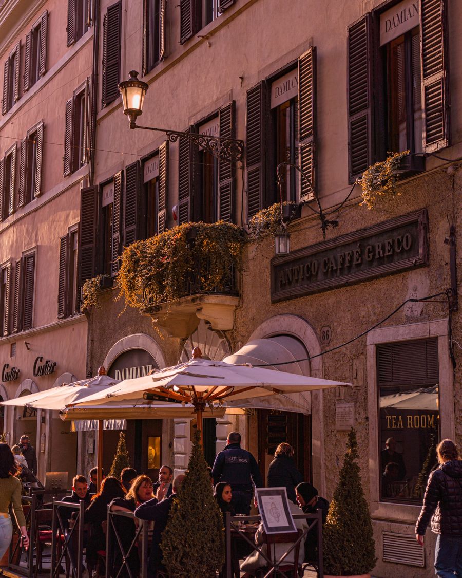 Umbrellas and outdoor tables beneath the Antico Caffè Greco sign in Rome