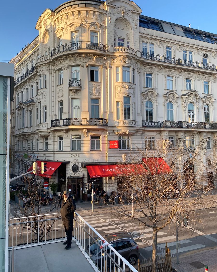 A grand corner building with red café awnings in Vienna, lit by the setting sun