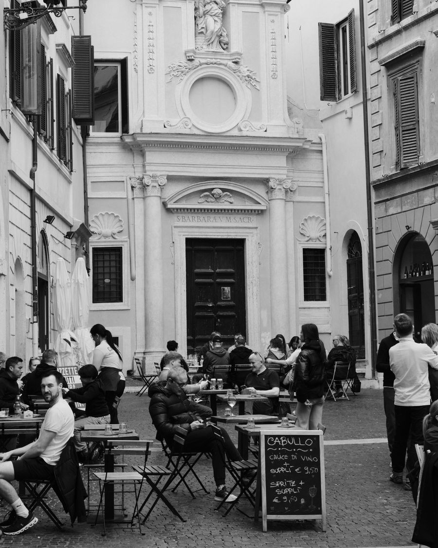 Black and white photo of people at outdoor café tables on a street in Rome