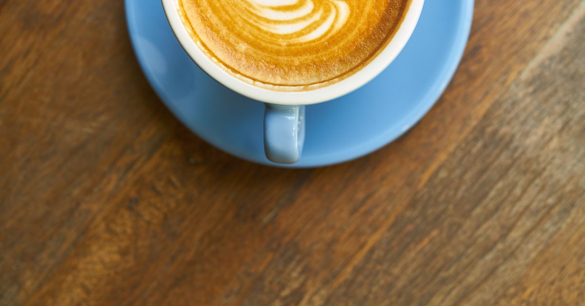 A cappuccino in daylight on a wooden café table, on why coffee beats cocktails for a first meet
